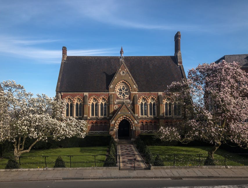 An outdoor scene featuring a paved pathway leading towards a historic church with a tall, pointed spire. The church has stone walls and arched windows, and is partially obscured by surrounding green t