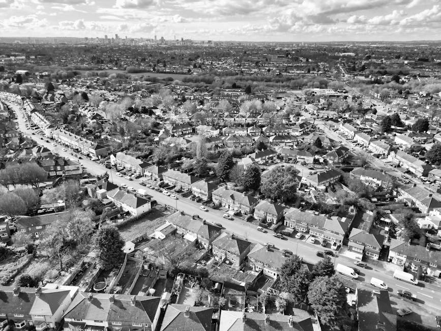 An aerial black-and-white photograph of a residential neighbourhood showing a variety of detached and semi-detached houses with pitched roofs, some with chimneys, and well-maintained gardens. The home